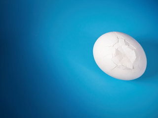 a whole white unpainted egg with cracks on a blue gradient background