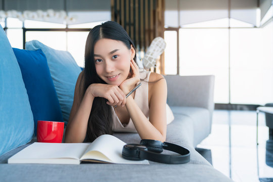 attractive  beautiful asian female smart casual relax enjoy working from home socail distacing quarantine on sofa ,asian female happiness with private moment working on sofa home background