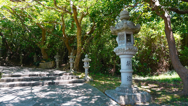 ancient Japanese statues, lanterns on the road through the jungle to a Buddhist temple. creepers and jungle over the road to a Japanese traditional religious temple. ancient temple on  island Okinawa