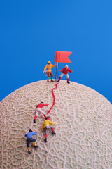 Miniature toys - a group of mountain climbers reaching to the top. Rock melon fruit as the base.