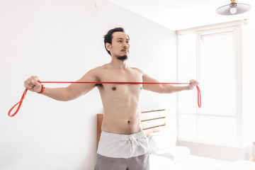 Fototapeta premium Asian man stretching his muscle in concept of workout at home with resistance band.
