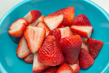 Freshly washed and sliced strawberries laying in a blue ice cream bowl