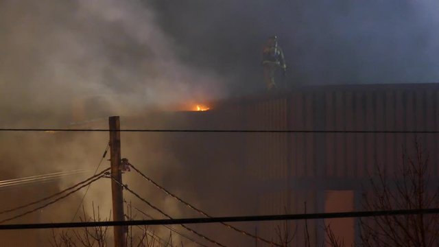 Fire fighter moving slowly towards source of fire while standing on roof