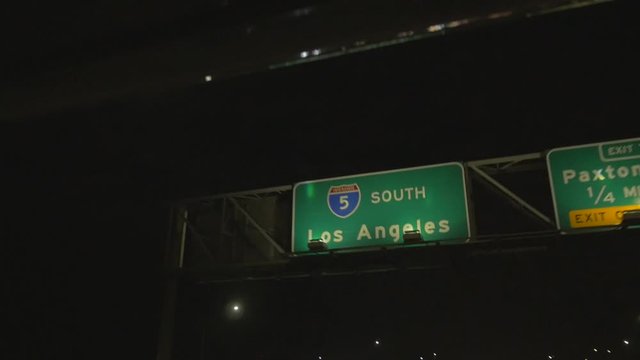Slow motion upward driving view of freeway sign in east Los Angeles California USA . Driving into Los angeles cinematic shot of a road sign, traffic LA arrival, drive in, entry, highway at night.