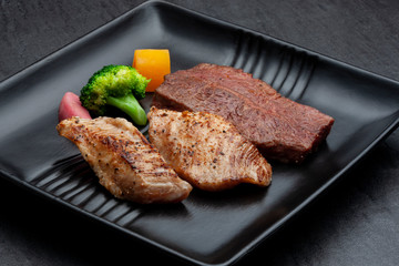 Grilled Chicken and Beef steaks  with on black ceramic plate.

