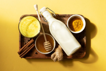 Turmeric milk and the ingredients for making the drink are on a wooden tray. Yellow background and top view. Natural light and shade