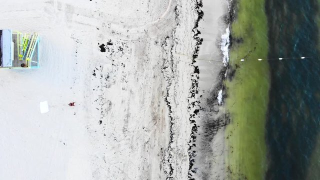 Bird's eye view drone shot of lifeguard tower, beach and gentle waves lapping the shore.