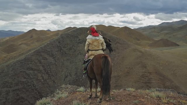 Kazakh golden eagle hunter on horse overlooking Altai Mountains peaks, Mongolia