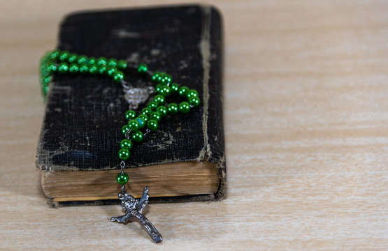 Old religious book with rosary and green crucifix on top on cla background...