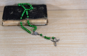 Old religious book with rosary and green crucifix on top on cla background...