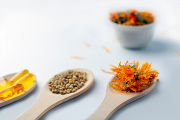 Herbal capsule, natural vitamins, dry calendula flowers at wooden spoon on white background. Concept of healthcare and alternative medicine: homeopathy and naturopathy. Close up, copy space for text