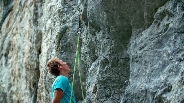 Athletic man attaching a rope to a quickdraw while preparing for rock climbing.