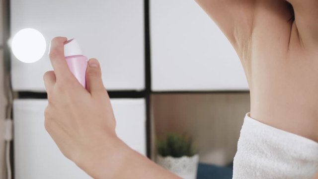 Girl uses deodorant. Young attractive woman in white towel in bathroom with her left hand sprays deodorant on her right armpit. Hygiene, skin care, freshness concept. Close-up