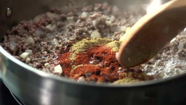 Spices get mixed into ground beef and onion in a skillet all in slow motion.