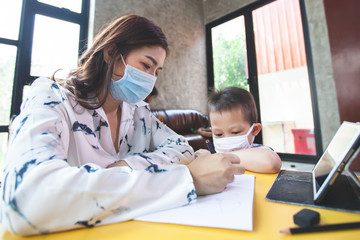 Work from home. Mother teaching and playing with her son while they quarantine for Coronavirus COVID-19. Mother and son wearing protective mask while working at home during coronavirus outbreak.