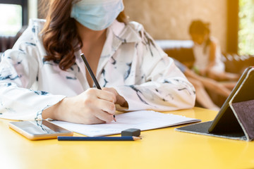 Work from home.Woman in quarantine for Coronavirus COVID-19 wearing protective mask writing on notebooks working at home while her kids playing at home during coronavirus outbreak