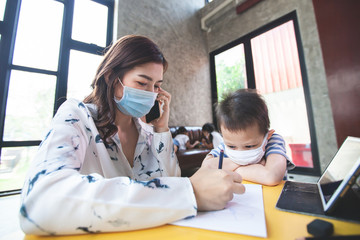 Work from home. Mother talking on phone and playing with son while they quarantine for Coronavirus COVID-19. Mother and son wearing protective mask while working at home during coronavirus outbreak.