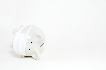 Upside down white piggy bank wearing surgical mask on white background with copy space. Concept for money saving plan, healthcare insurance, coronavirus economic crisis, or financial accounting