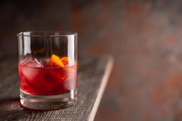 Red traditional old fashioned cocktail with orange zest on the rustic background. Selective focus. Shallow depth of field.