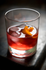 Red traditional old fashioned cocktail with orange zest on the rustic background. Selective focus. Shallow depth of field.