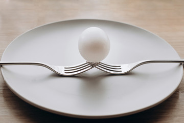 one whole white egg on 2 forks against a light plate