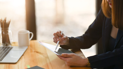 Fototapeta premium Closeup businesswoman holding a computer tablet and stylus pen while sitting at the wooden working desk over comfortable sitting room as background.