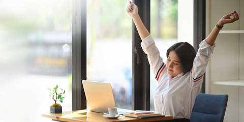 Gorgeous office woman relaxing by stretching her body while sitting in front her computer laptop at...