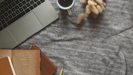 Top view image of Computer laptop, Old books, Coffee cup and Wild grass putting together on working table that cover with grey tablecloth as background.