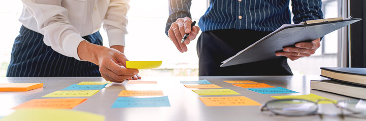 Business people arranging sticky notes commenting and brainstorming on work priorities colleague in a modern co-working space.