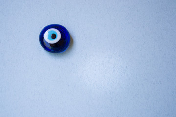 Glass Turkish eye "Nazar Boncugu" on blue background, object, superstition concept, indoors