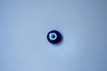Glass Turkish eye "Nazar Boncugu" on blue background, object, superstition concept, indoors
