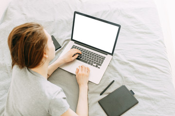 The girl works at home on the sofa with a laptop. The girl works from home lying on the bed. Online earnings during the quarantine.