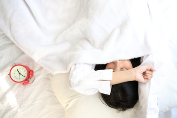 Asian woman lazy sleep waking up on bed with clock in white bedroom