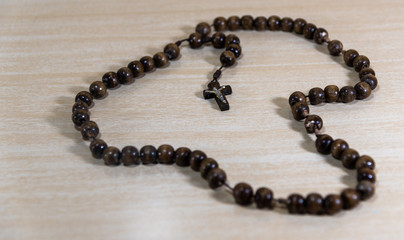 Rosary and crucifix symbols of Catholicism on light wooden background