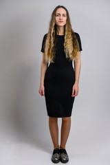 Full-length portrait of a pretty young woman in a black dress with a good figure with long hair. Model stands on a white background.