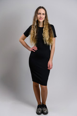 Full-length portrait of a pretty young woman in a black dress with a good figure with long hair. Model stands on a white background.