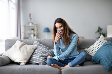 Smiling woman with smartphone at home on the couch. Online shoping.