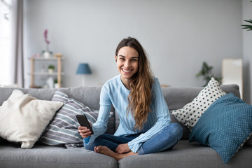 Smiling woman with smartphone at home on the couch. Online shoping.