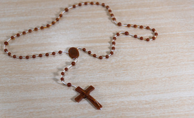 Rosary and crucifix symbols of Catholicism on light wooden background