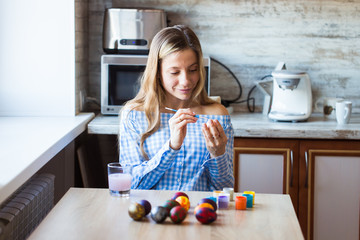 Holidays, handmade and creation concept - Happy young woman draws on Easter egg.