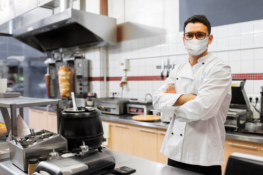 health protection, safety and pandemic concept - male chef cook wearing face protective medical mask over kebab shop kitchen background