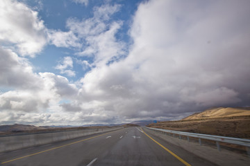 Asphalt road and bright blue sky with fluffy clouds . Empty desert asphalt road from low angle with mountains and clouds on background. road, red desert landscape . Open road with blue clouds .