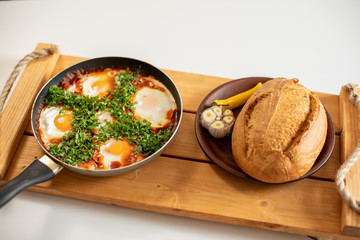 Shakshuka stands on a wooden table. Tasty shakshuka with bread. Top view. Close up.
