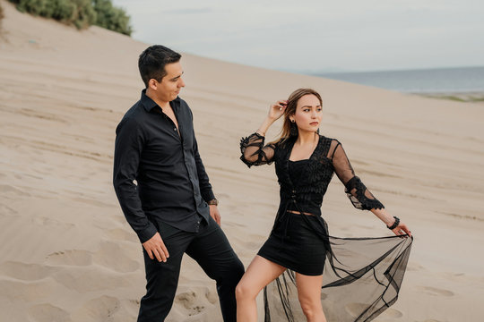 Pareja Hombre y Mujer elegantes vestidos de negro parados sobre la arena en la playa. 
Hombre mirando mujer 
Mujer mirando a un lado
Pareja enamorados
Pareja guapos