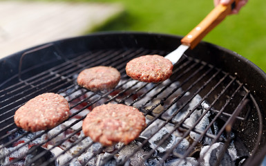 cooking, barbecue and fast food concept - close up of burger meat cutlets roasting on brazier grill outdoors