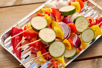 cooking, barbecue and food concept - close up of vegetables with champignons on skewers stacked on disposable foil grill on wooden table