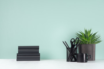 Fresh spring workplace for work and study with black stationery, books, coffee cup, aloe plant in light green mint menthe interior on white wood desk, copy space.