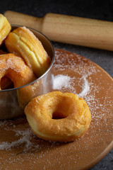 Donuts with sugar on a wooden plate over a dark table background.