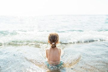 Fototapeta na wymiar Small girl is relaxing in the sea water with waves on the beach.Summer sunny day.Travel,summer and vacation concept.