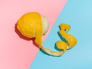 Lemon with spiral peeled zest over blue and pink minimalistic background. Lemon and peel in hard...